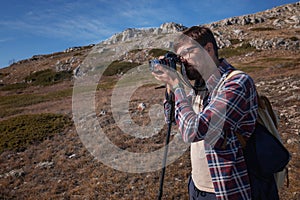 Young man taking photographs with digital camera in a mountains.