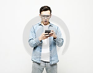 young cheerful man standing isolated over white background, using mobile phone
