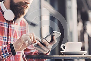 Young man texting on his smartphone in the city. Close up of cheerful adult using mobile phone in a cafe