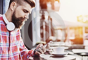 Young cheerful man using smartphone in the city. Close up of cheerful adult using mobile phone in a cafe