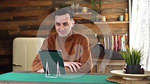 Young cheerful man using tablet computer having online video chat with friends.