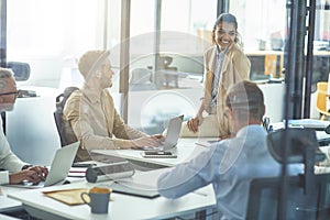 Young cheerful mixed race female office worker discussing something with colleagues while sitting in board room in the