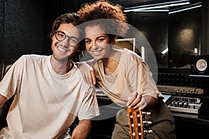 Young cheerful musicians happily looking in camera recording new song together in modern studio