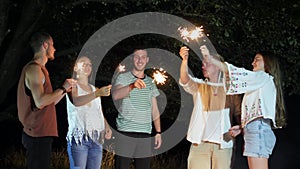 Young cheerful people sitting on the weekend at night with firework sparklers.