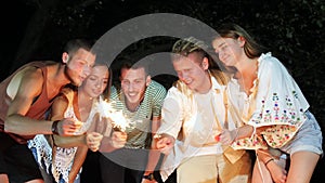 Young cheerful people sitting on the weekend at night with firework sparklers.