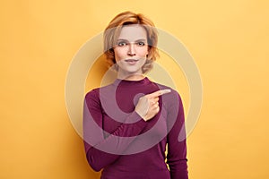 Young cheerful pleasant woman pointing side way by finger