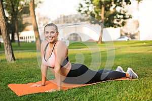 Young cheerful plus size woman in sporty top and leggings practicing yoga on orange yoga mat joyfully looking in camera
