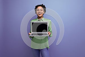 young cheerful positive hispanic brunette lady dressed in a green stylish blouse holds a laptop with a mockup on the