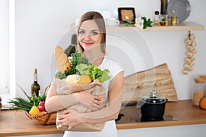 Giovane contento donna sorridente è un pronto cucinando la cucina. casalinga è un possesso il grande borsa pieno da fresco 