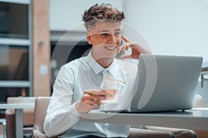 Young and cheerful Spanish man holding cash Euro and working on a computer