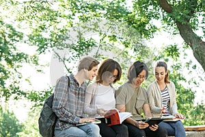 Young cheerful students sitting and studying outdoors