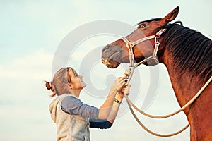 Young cheerful teenage girl calming big spirit chestnut horse.