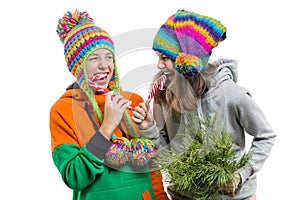 Young cheerful teenage girls having fun with Christmas candy canes, in winter knitted caps, isolated on white background