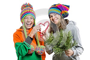 Young cheerful teenage girls having fun with Christmas candy canes, in winter knitted caps, isolated on white background