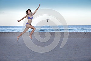 Young cheerful woman in bikini jumping on the beach.