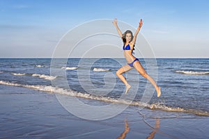 Young cheerful woman in bikini jumping on the beach.