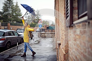 A young cheerful woman with a blue umbrella is dancing while walking the city on a rainy day. Walk, rain, city