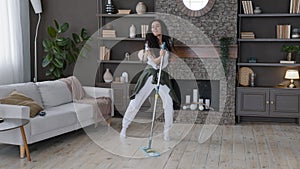 Young cheerful woman cleaning apartment washes floor in living room excited energetic girl dancing with mop comic motion