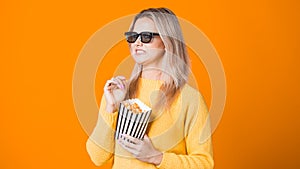 Young cheerful woman in 3D glasses watching a movie and eating popcorn.