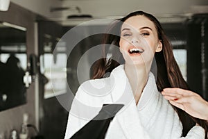 Young cheerful woman drying hair with blowdryer