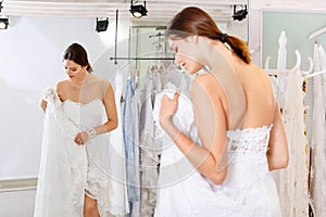Young cheerful woman fitting luxury wedding dress at modern wedding salon