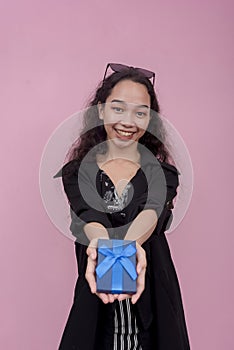 A young cheerful woman hands over a small gift, possibly jewelry inside a small wrapped blue box.