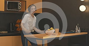 Young cheerful woman in headphones dancing in kitchen and leaving with apple. Portrait of joyful carefree Caucasian lady