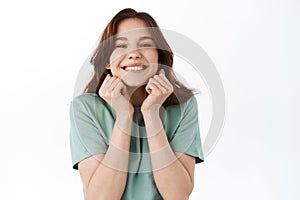 Young cheerful woman looking with pleased and happy face, rejoicing from compliments and praises, standing against white