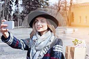 Young cheerful woman posing while photographing herself on smart phone camera for a chat with friends, attractive smiling hipster