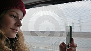 Young cheerful woman in a red hat, traveling by bus on a sad day. She takes pictures on a smartphone
