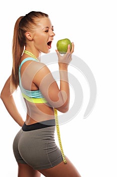 Young cheerful woman in sports wear with green apple on white background