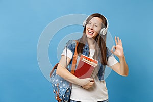 Young cheerful woman student in denim clothes with backpack headphones listen music hold school books showing OK sign