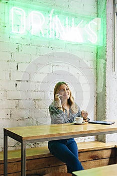 Young cheerful woman talking to her phone on her coffee break