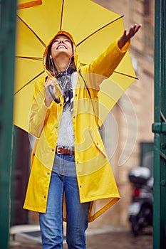 A young cheerful woman with a yellow raincoat and umbrella who is enjoying the rain while walking the city on a cloudy day. Walk,