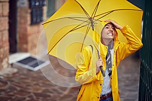 A young cheerful woman with a yellow raincoat and umbrella who is in a good mood while walking the city on a rainy day. Walk, rain