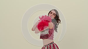 Young cheerleader with red pompoms in uniform is dancing on white background in studio. Beautiful cheerleader performs