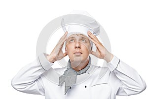 Young chef adjusts his hat on his head on a white