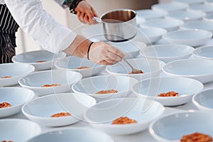 Young chef cook putting tomato sauce on dishes