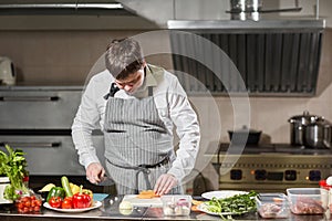 Young chef cutting beet on a white cutting board closeup. Cooking in a restaurant kitchen