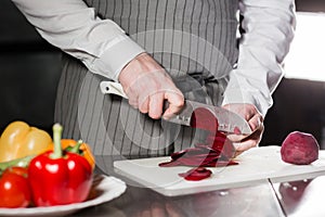 Young chef cutting beet on a white cutting board. Closeup of hand with knife cutting fresh vegetable. Cooking in a