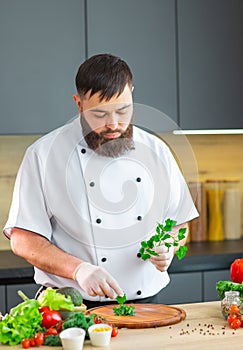 Young chef is cutting herbs and parsley in a modern kitchen. The man prepares food at home. Cooking healthy and tasty