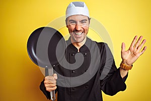 Young chef man wearing uniform and hat holding cook pan over isolated yellow background very happy and excited, winner expression