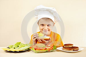 Young chef puts salad on big sandwich