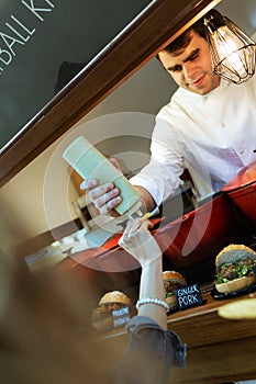 Young chef serving mayonnaise on a customer`s potatoes in a food truck.