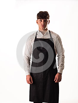 Young chef or waiter posing, wearing black apron and white shirt isolated