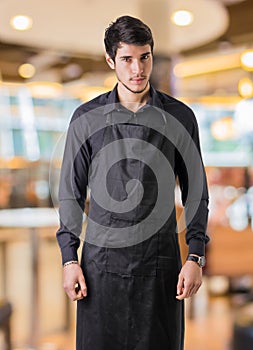 Young chef or waiter wearing black apron in restaurant