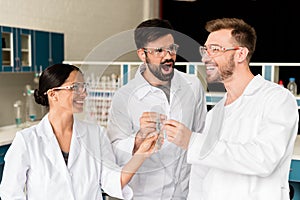 Young chemists clinking test tubes with reagents in lab