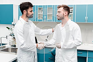 Young chemists in white coats shaking hands in scientific laboratory