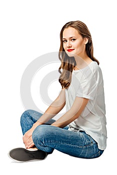 Young cherful woman in jeans, white t-shirt, sneakers sits on the floor and smiles. isolated on white background photo