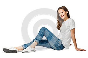 Young cherful woman in jeans, white t-shirt, sneakers sits on the floor and smiles.  on white background